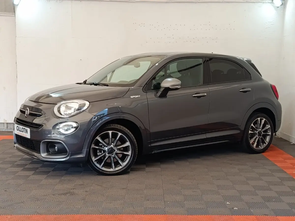 Fiat 500X gris foncé vue de profil droit en intérieur, avec jantes alliage et rétroviseurs argentés.