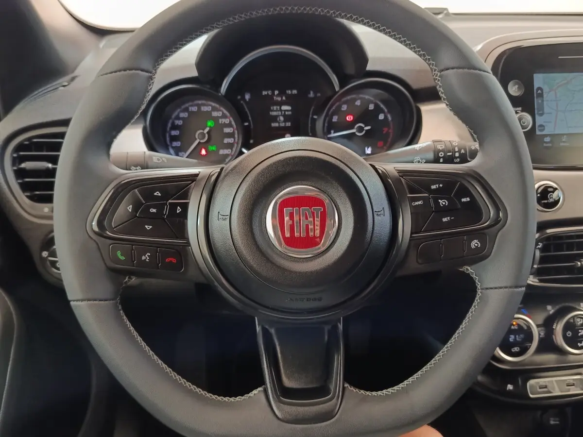 Vue rapprochée du volant cuir gris avec logo FIAT rouge et tableau de bord numérique de la 500X 2021.