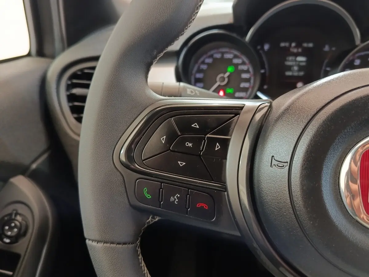 Gros plan sur les commandes gauche du volant cuir de la FIAT 500X gris foncé, avec tableau de bord en arrière-plan flou.