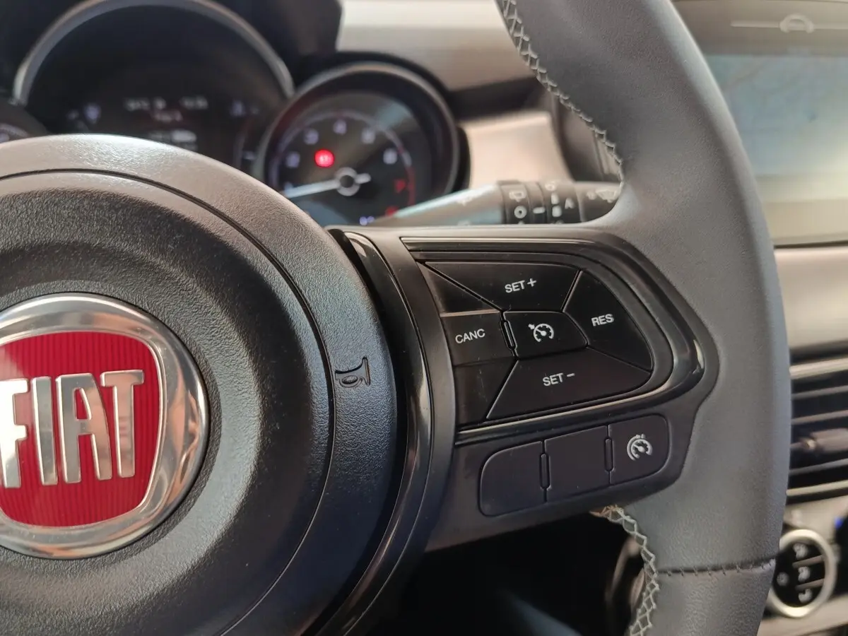Vue rapprochée du volant cuir noir de la FIAT 500X 2021 avec commandes de régulateur de vitesse et logo rouge FIAT.
