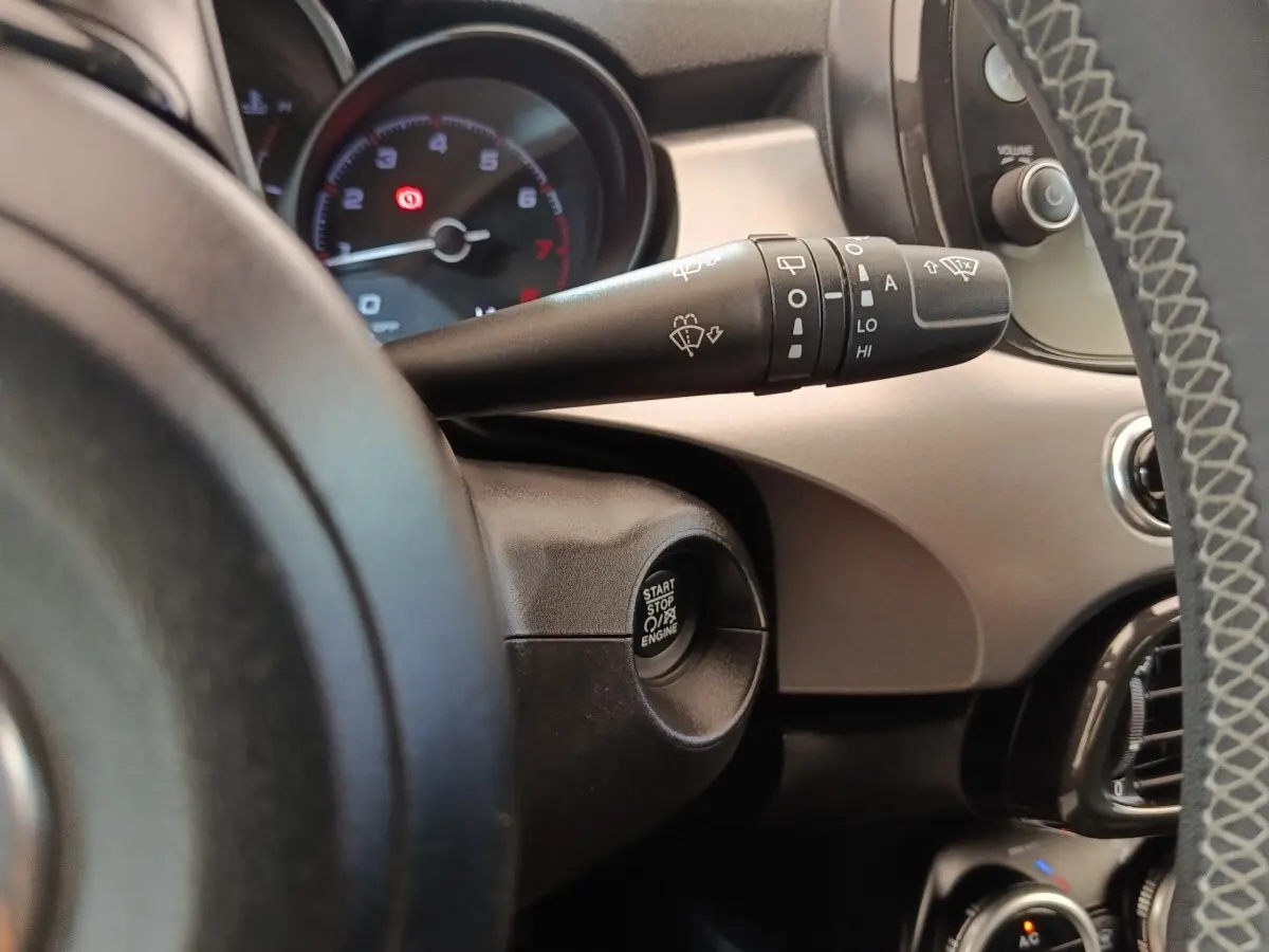 Gros plan intérieur sur le bouton démarrage et la commande d’essuie-glace à gauche du volant d’une Fiat 500X gris foncé.