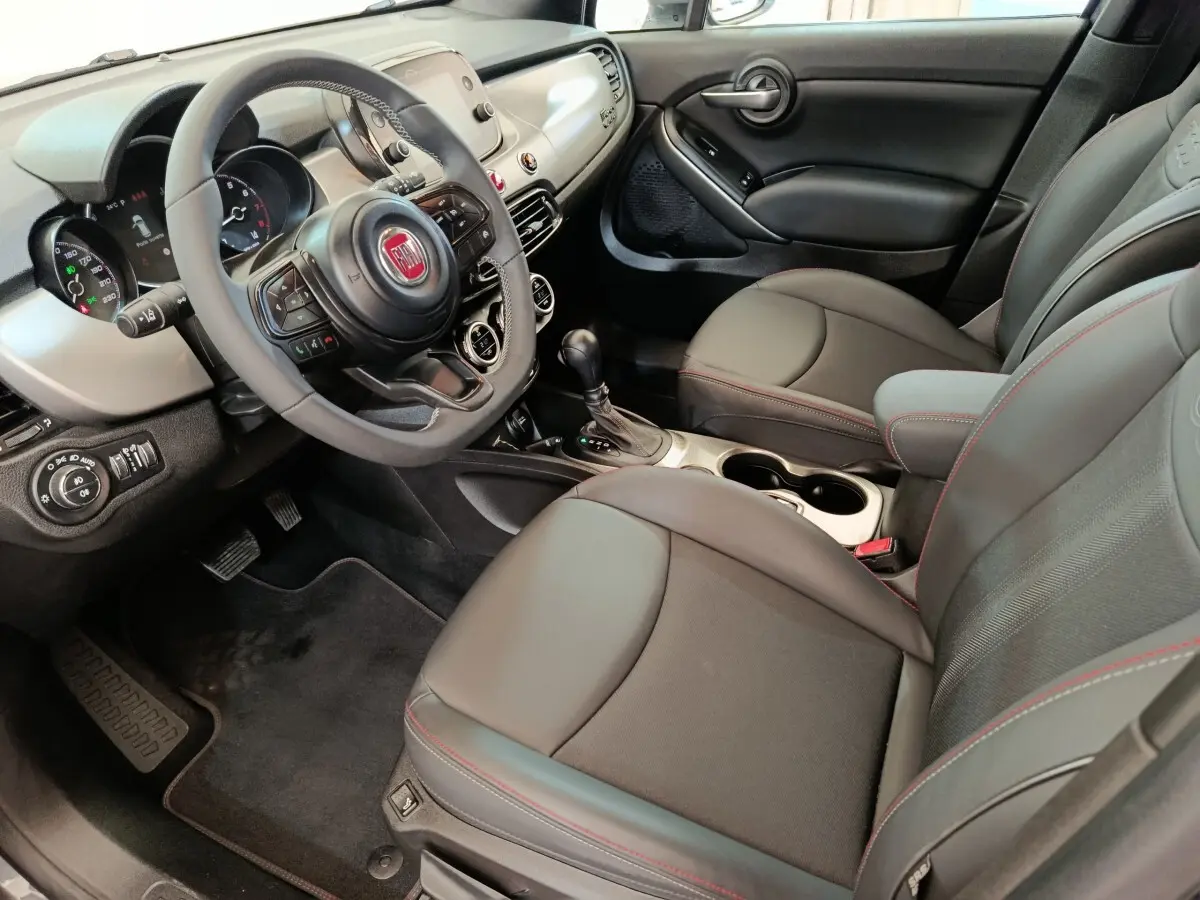 Intérieur avant droit de la Fiat 500X gris foncé, volant multifonctions, sièges cuir noir avec surpiqûres rouges.