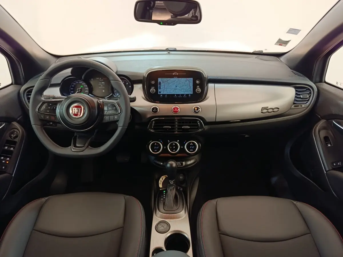 Vue intérieure avant de la Fiat 500X 2021, tableau de bord gris clair avec écran tactile et volant multifonctions noir.