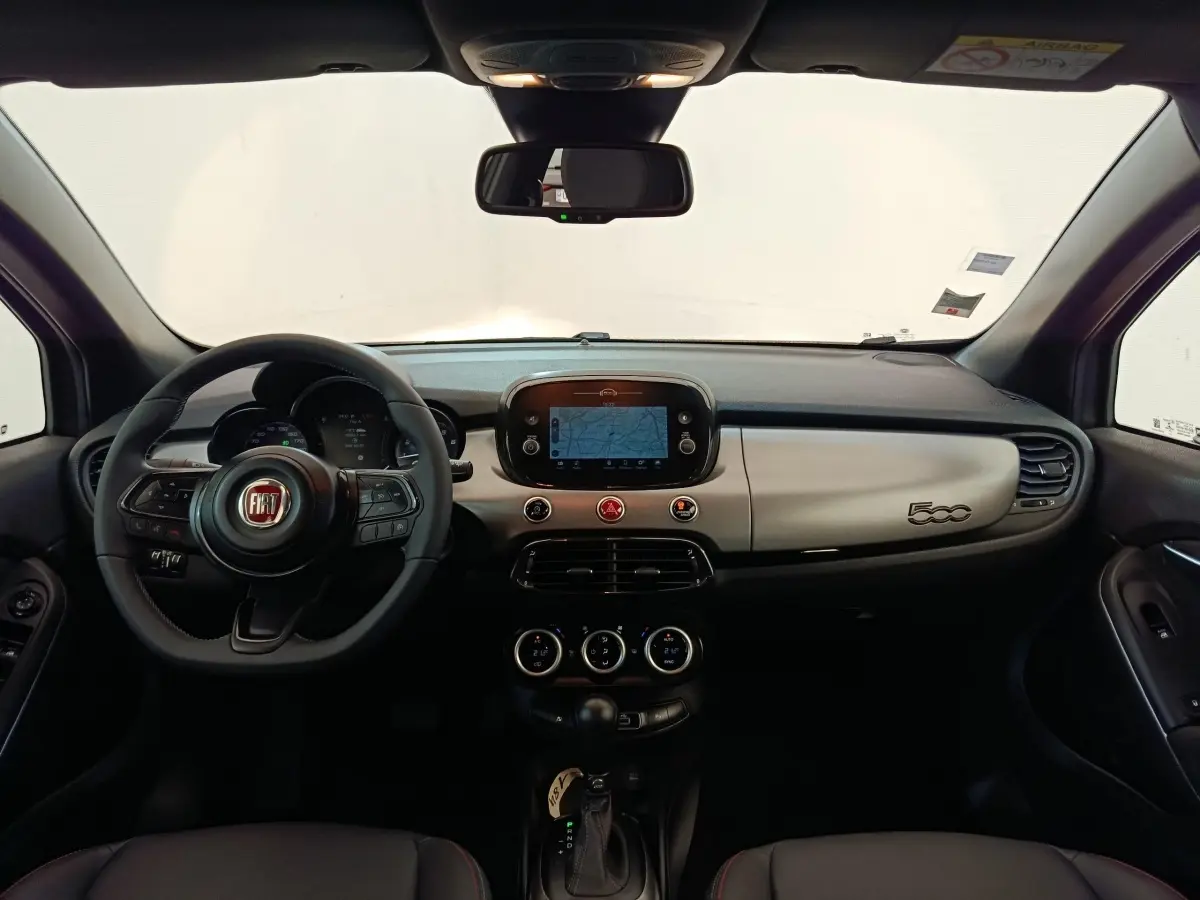 Vue intérieure frontale du tableau de bord gris clair et noir de la FIAT 500X 2021 avec écran tactile et volant multifonctions.