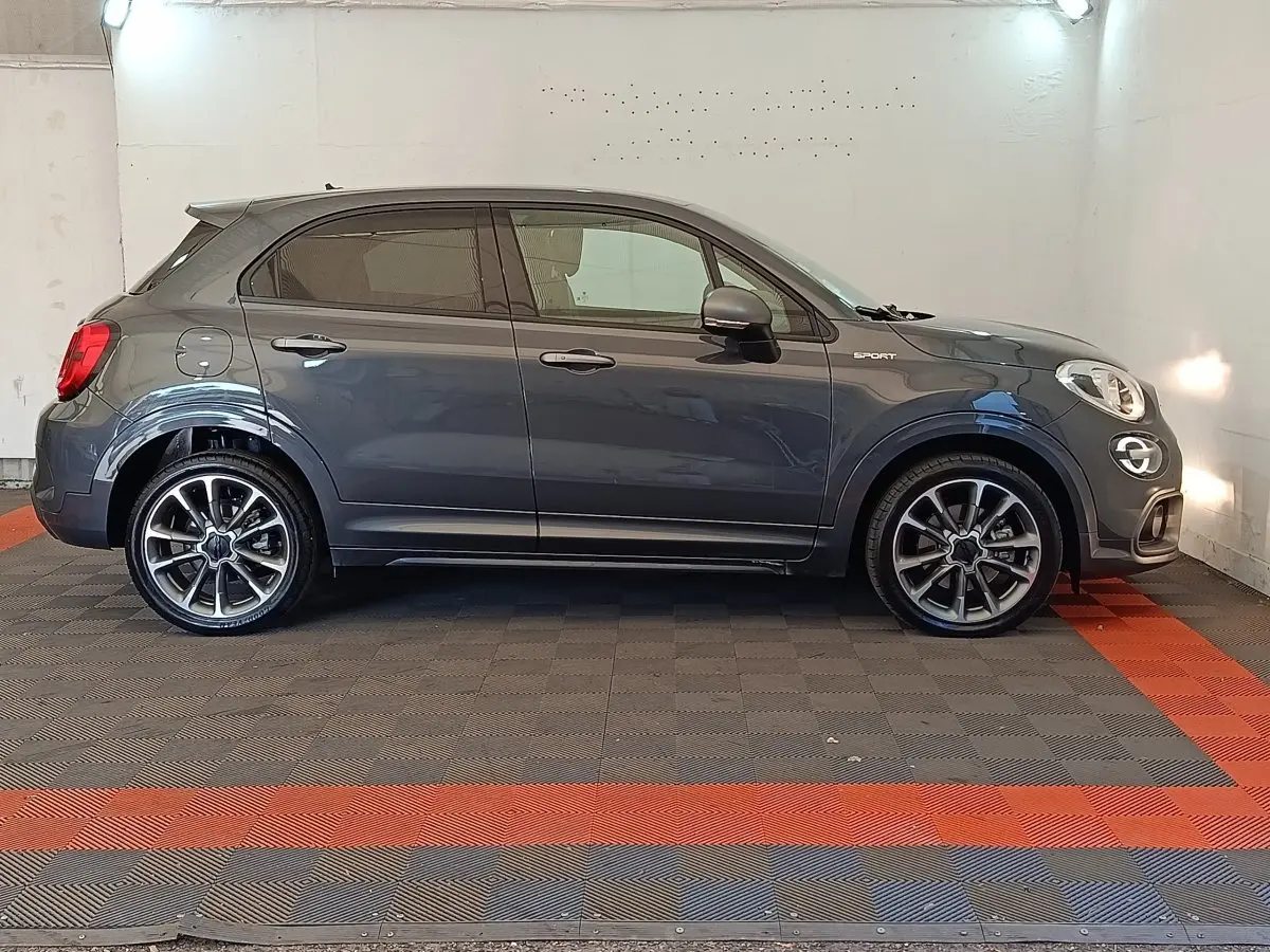 Profil droit d'une FIAT 500X Sport gris foncé avec jantes alliage et rétroviseurs ton caisse, en intérieur.