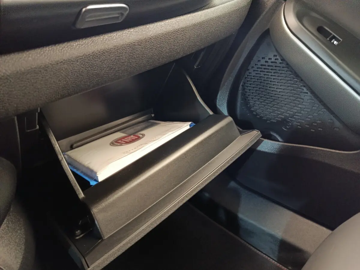 Vue intérieure côté passager du coffre à gants ouvert avec manuel FIAT visible dans un Fiat 500X gris foncé.
