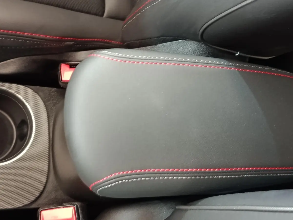 Détail de l'accoudoir central noir avec surpiqûres rouges dans l'habitacle de la Fiat 500X gris foncé.