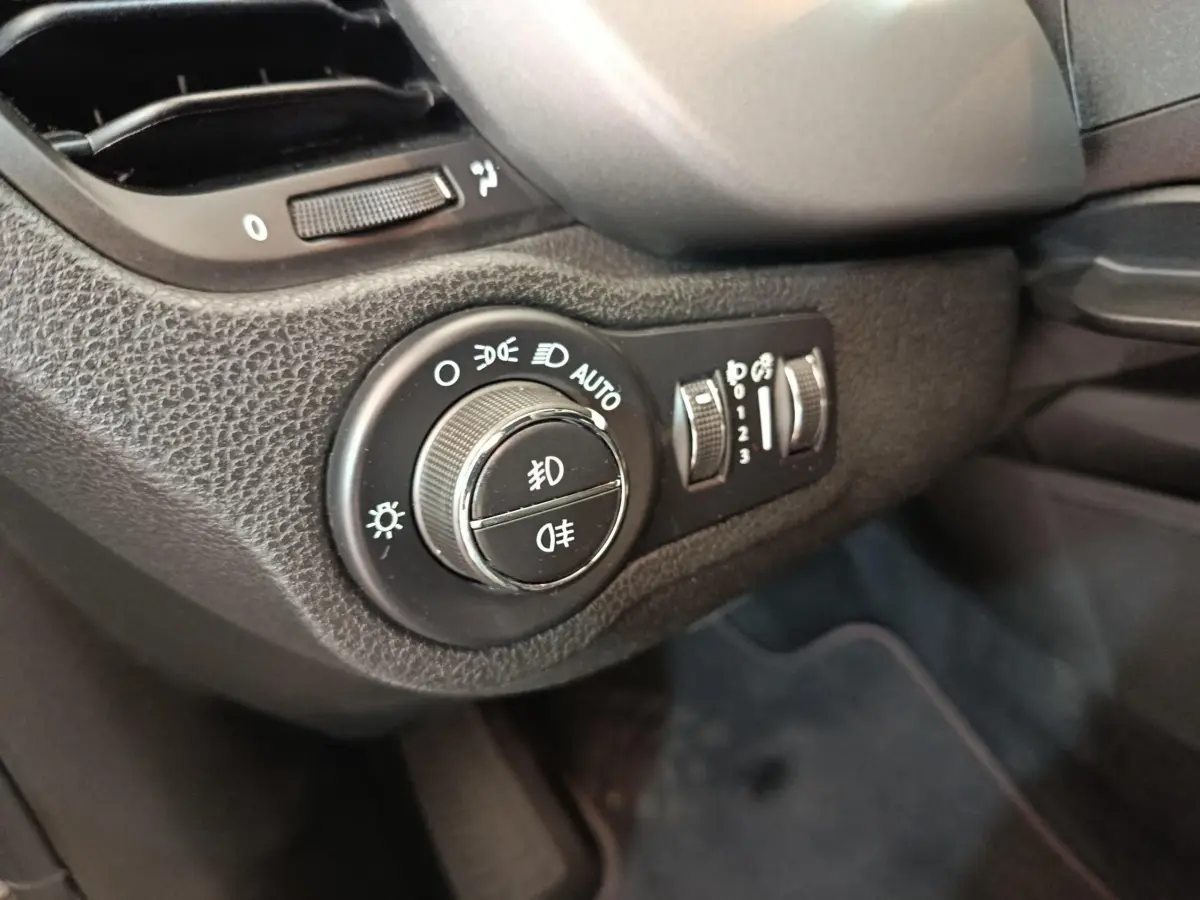 Gros plan sur la molette de réglage des phares et commandes d’éclairage intérieures d’une Fiat 500X gris foncé, côté conducteur.