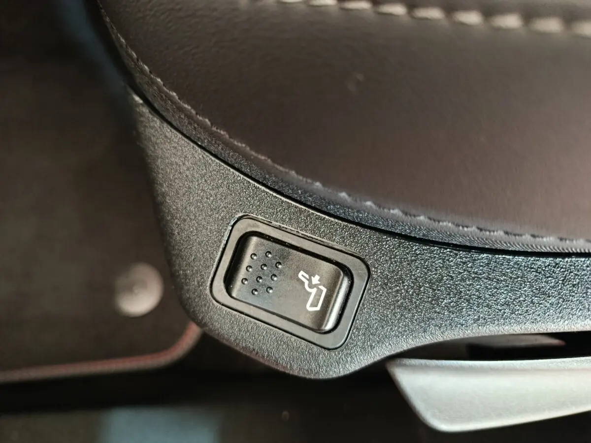 Bouton de réglage électrique de siège en gros plan sur l'assise en cuir marron foncé d'une Fiat 500X gris foncé.
