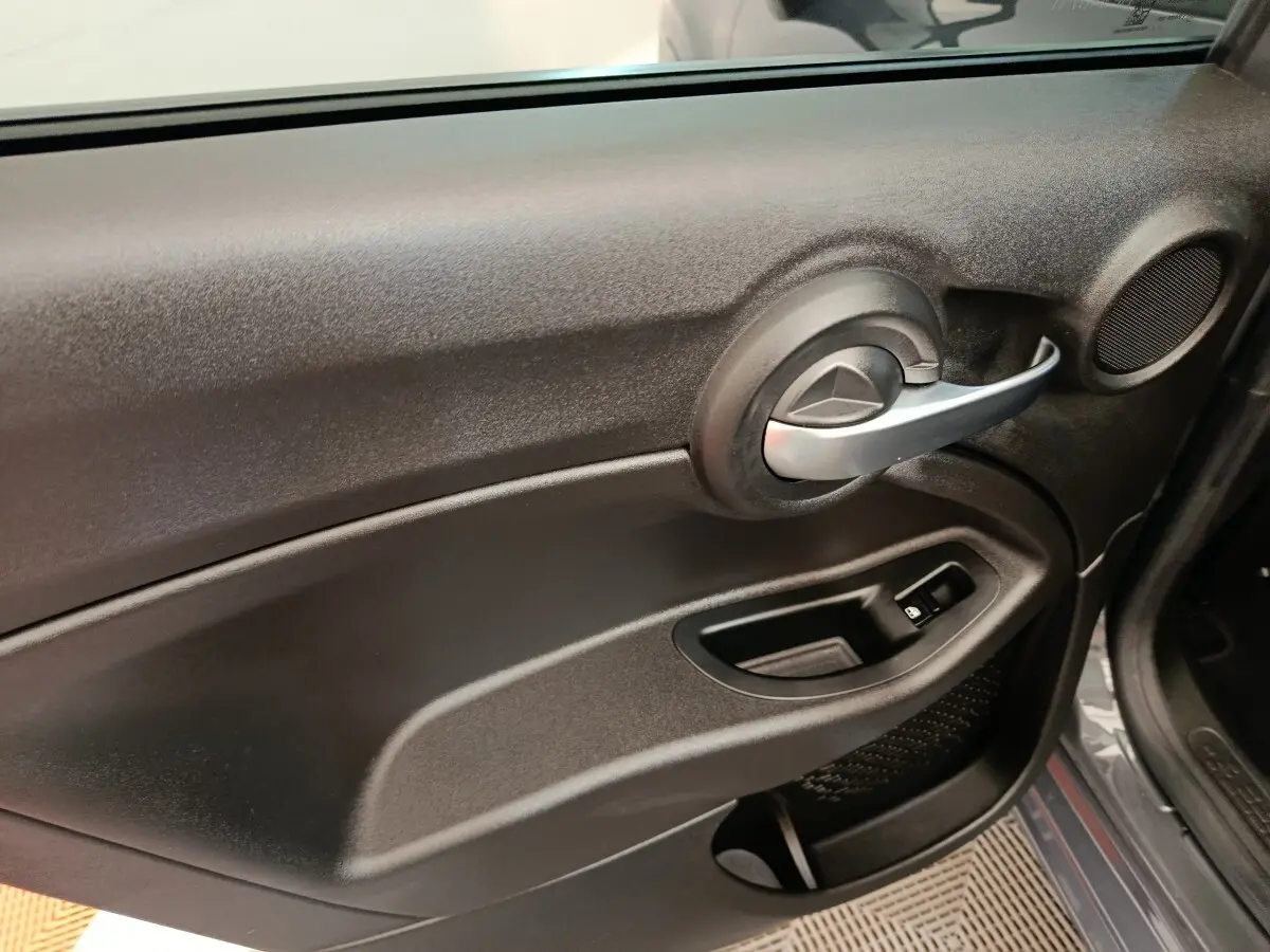 Vue intérieure côté gauche de la porte avant d’une FIAT 500X gris foncé avec poignée argentée et commande de vitre électrique.