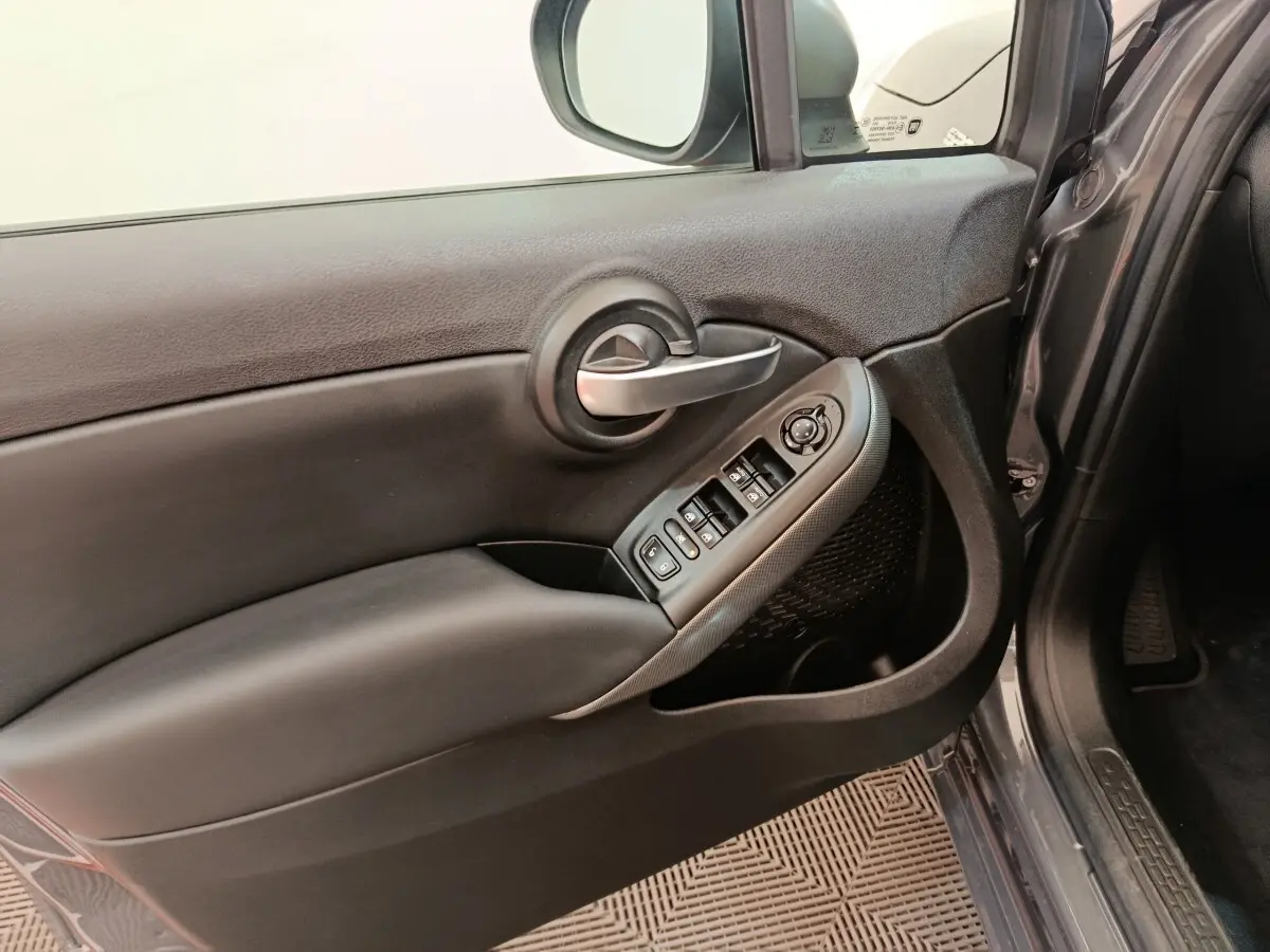 Intérieur côté conducteur de la FIAT 500X gris foncé, montrant la porte avec commandes des vitres et rétroviseur.