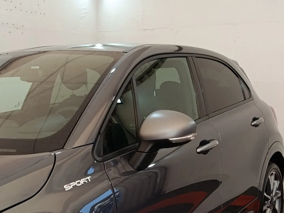 Vue de côté droit avant d'une FIAT 500X gris foncé avec badge Sport et rétroviseur assorti.