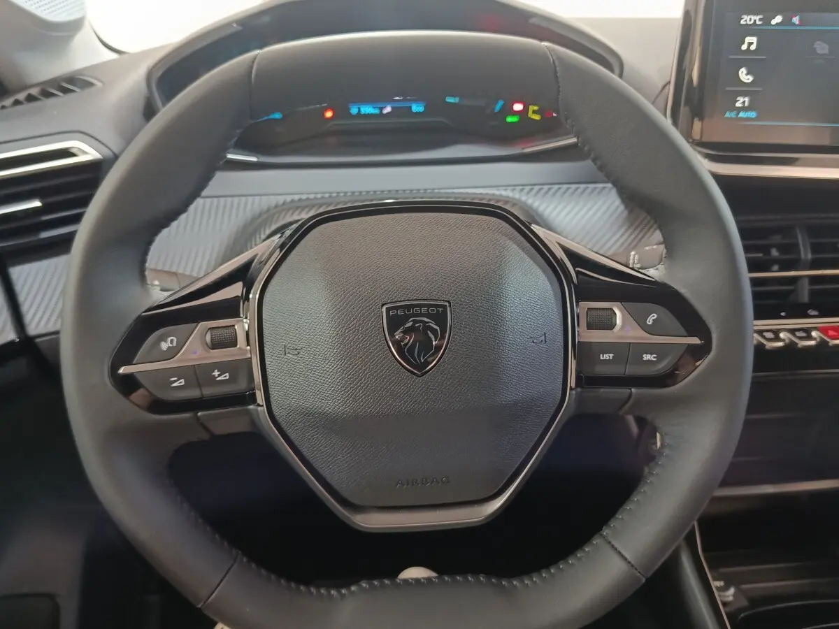 Vue rapprochée du volant cuir multifonctions noir de la Peugeot 208 électrique 2024 avec tableau de bord numérique en arrière-plan.