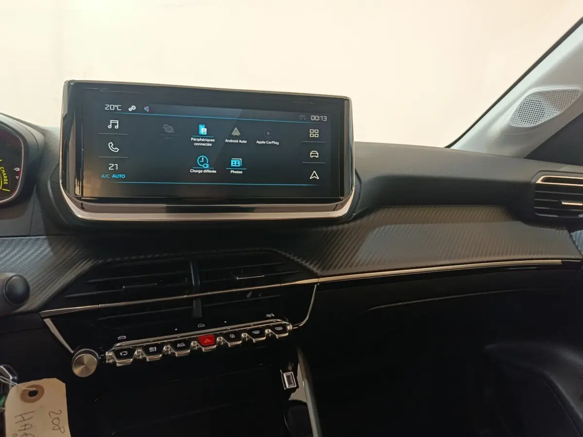 Vue intérieure du tableau de bord de la Peugeot 208 électrique 2024 avec écran tactile central et finition carbone gris.