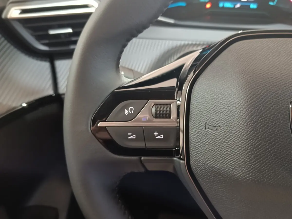 Gros plan sur le côté gauche du volant cuir noir du Peugeot 208 électrique 2024 avec commandes multifonctions.