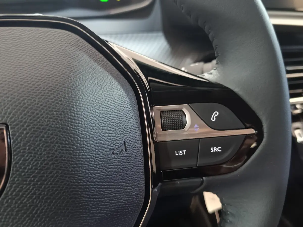 Gros plan sur le volant cuir multifonctions côté droit du Peugeot 208 électrique 2024, avec commandes intégrées.