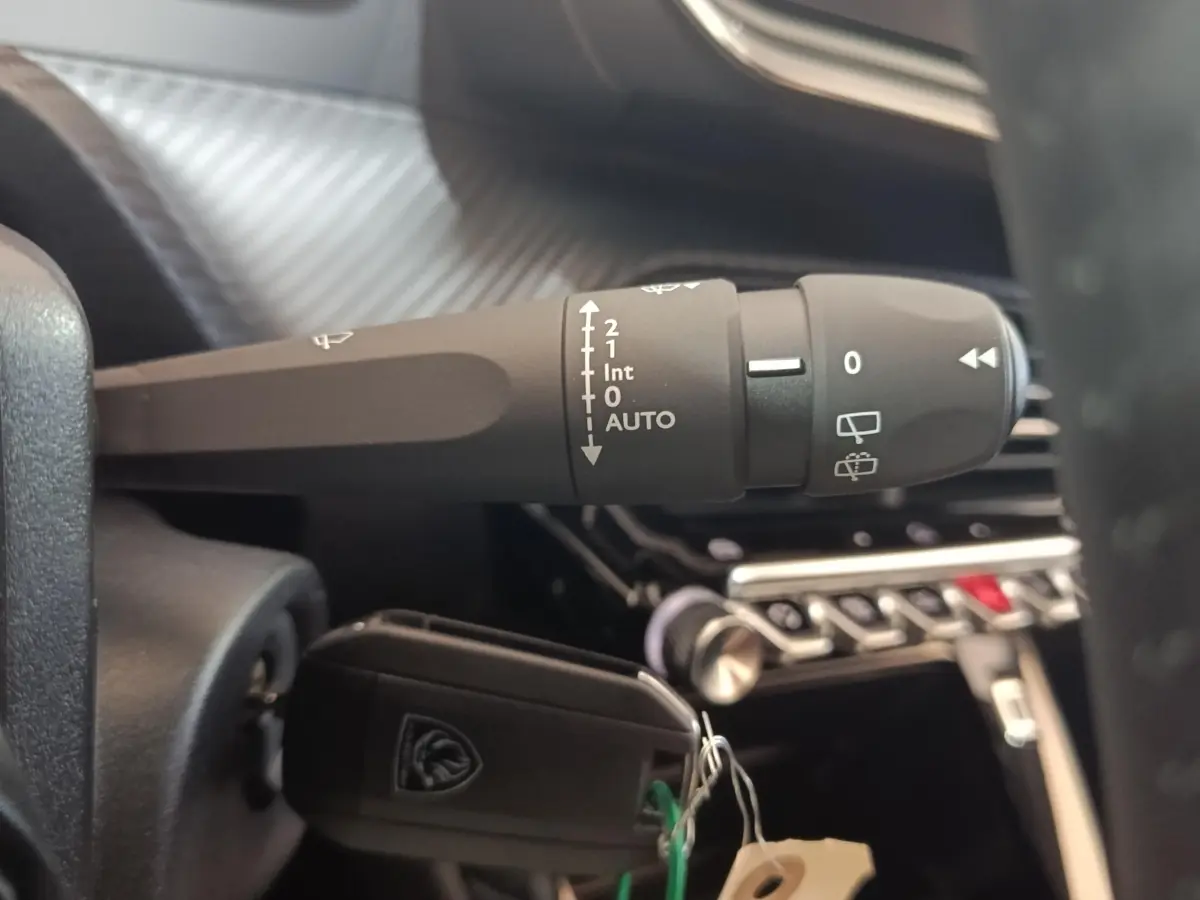 Gros plan sur la commande des essuie-glaces et clé insérée dans le contact d'un Peugeot 208 électrique gris clair, intérieur moderne.