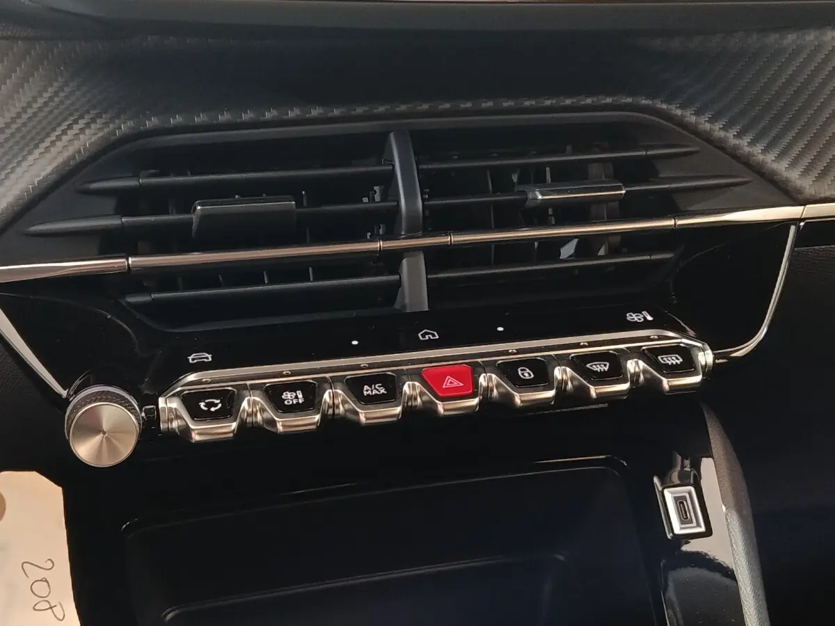 Détail du tableau de bord de la Peugeot 208 électrique 2024 montrant les commandes centrales et les aérateurs noirs.
