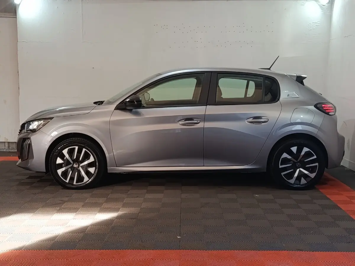 Profil côté gauche d'une Peugeot 208 électrique gris clair, avec jantes modernes et feux arrière LED allumés.