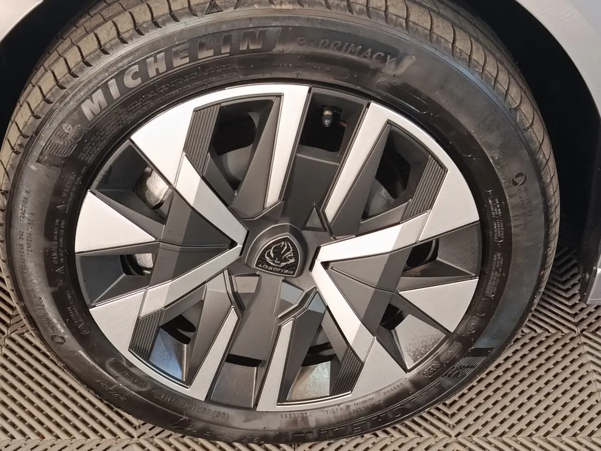 Gros plan sur la roue avant droite d’une Peugeot 208 électrique gris clair, jante au design géométrique moderne.