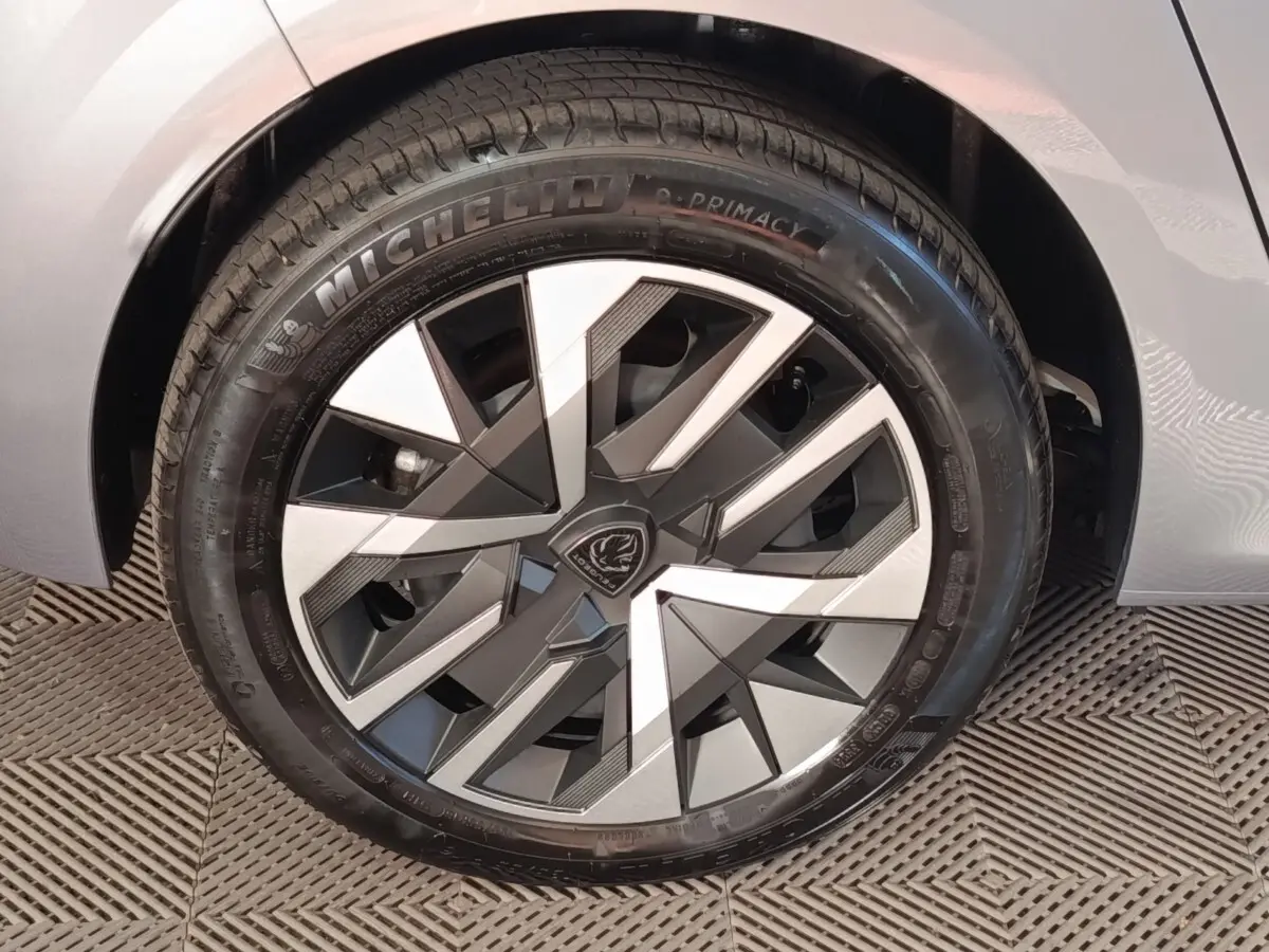 Gros plan sur la roue avant droite d'une Peugeot 208 électrique gris clair, avec jante au design géométrique moderne.