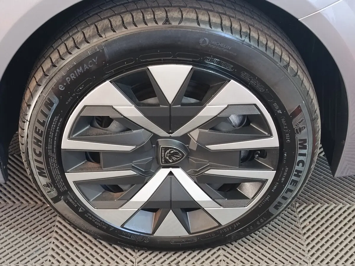 Gros plan sur la roue avant droite gris clair d'une Peugeot 208 électrique 2024 avec jante au design géométrique bicolore.