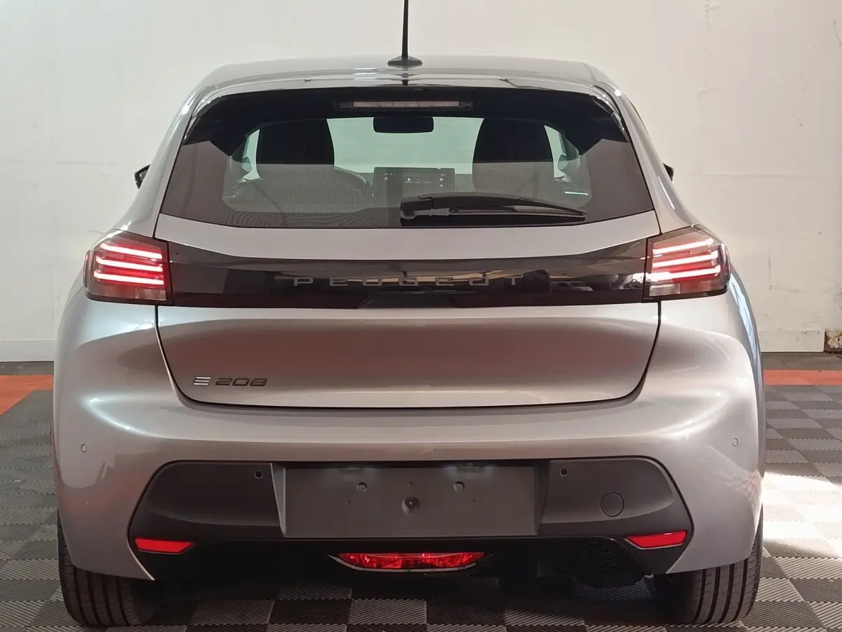 Vue arrière d'une Peugeot 208 électrique gris clair avec feux LED et logo PEUGEOT lumineux sur la malle.
