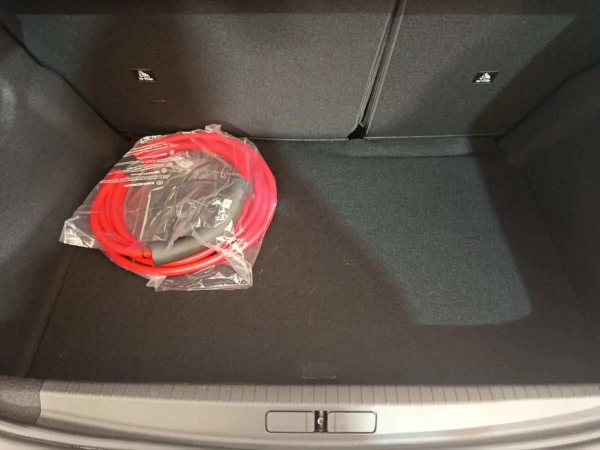 Coffre de Peugeot 208 électrique gris clair vu de dessus, avec câble de recharge rouge emballé posé à gauche.