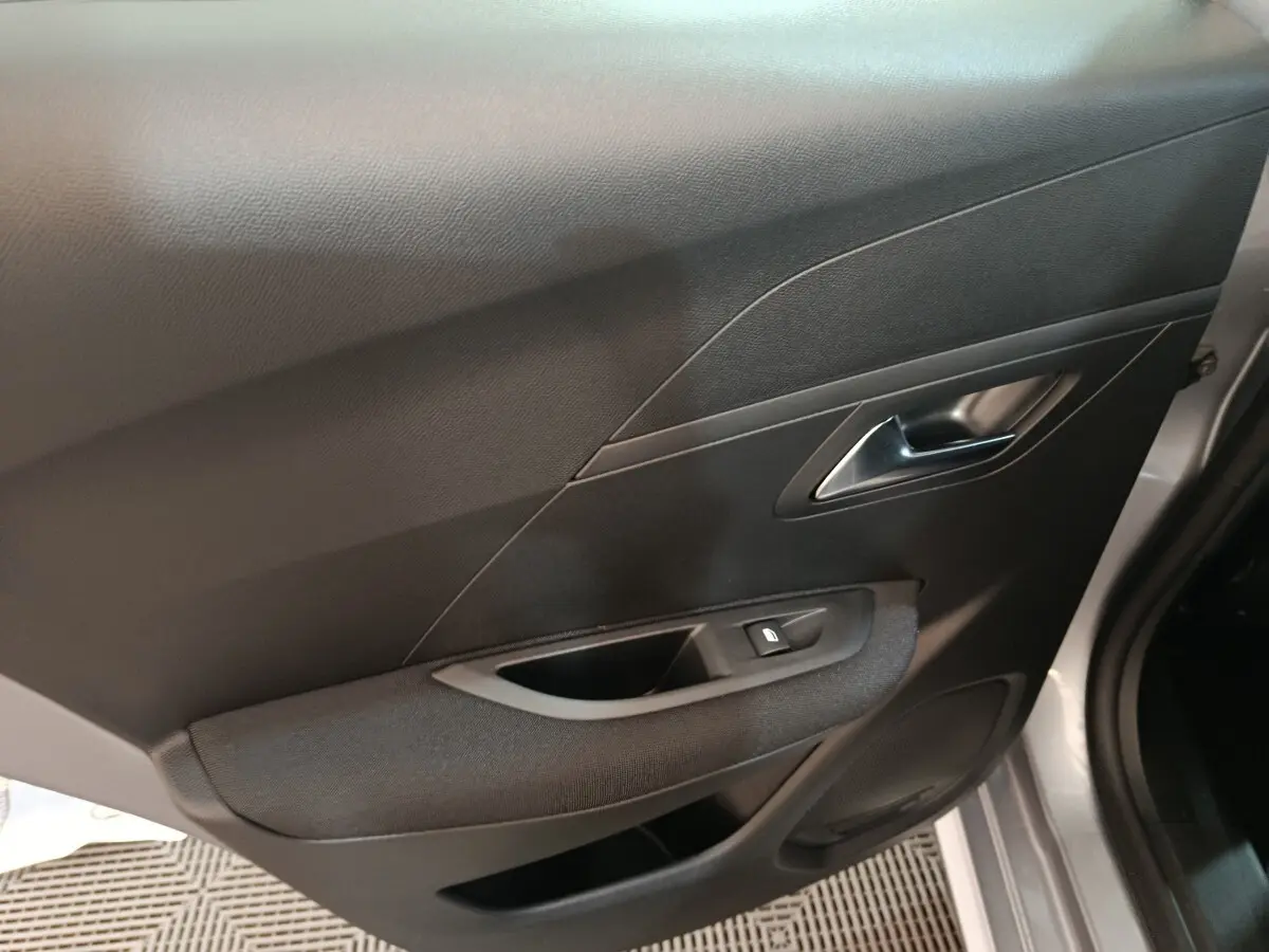 Vue intérieure côté droit de la porte avant d'une Peugeot 208 électrique gris clair avec bouton de lève-vitre et poignée métallique.