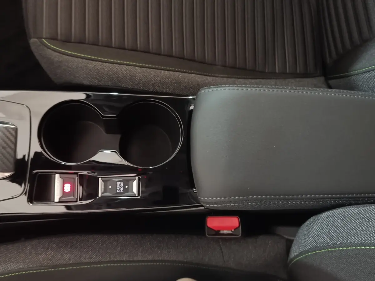 Vue intérieure rapprochée du tunnel central noir brillant avec accoudoir cuir et porte-gobelets de la Peugeot 208 électrique gris clair.