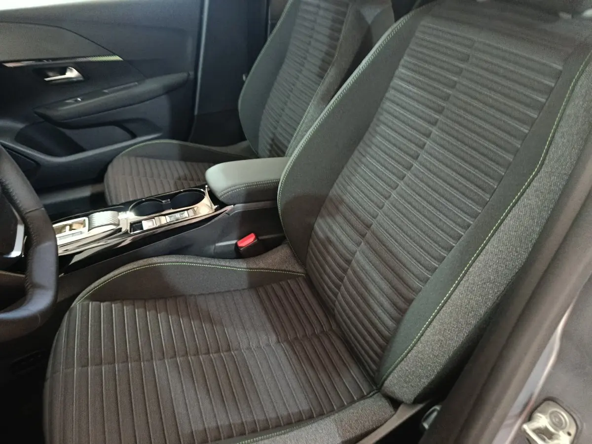 Vue intérieure côté conducteur de la Peugeot 208 électrique 2024, sièges tissu gris foncé avec surpiqûres vertes et console centrale.