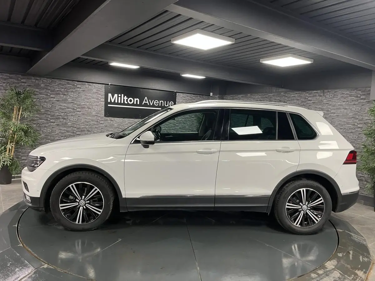 Vue de profil côté gauche d'un Volkswagen Tiguan blanc avec jantes alliage noires et décorations noires basses.