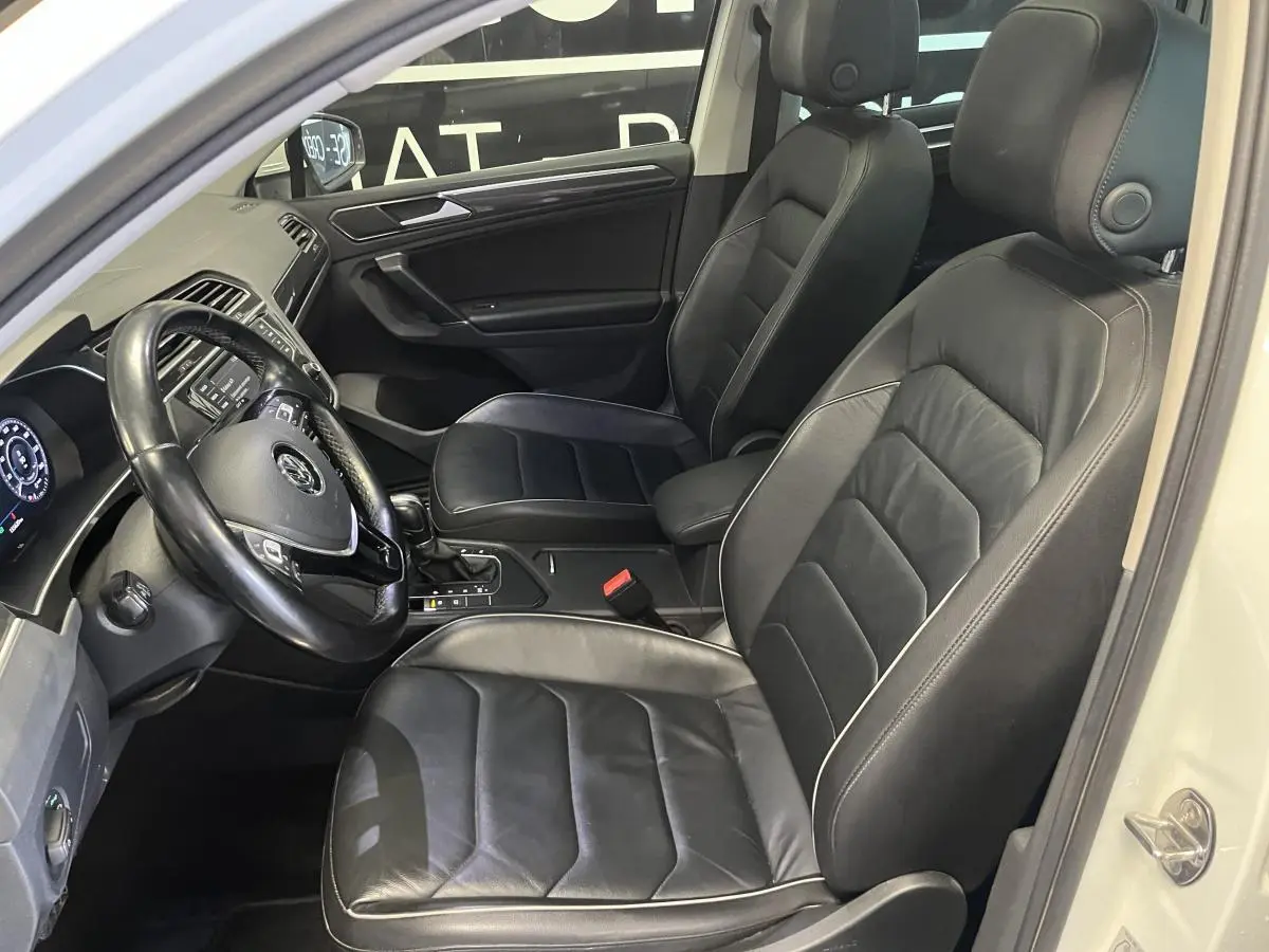 Vue intérieure côté conducteur du Volkswagen Tiguan 2017 avec sièges sport en cuir noir et tableau de bord digital.