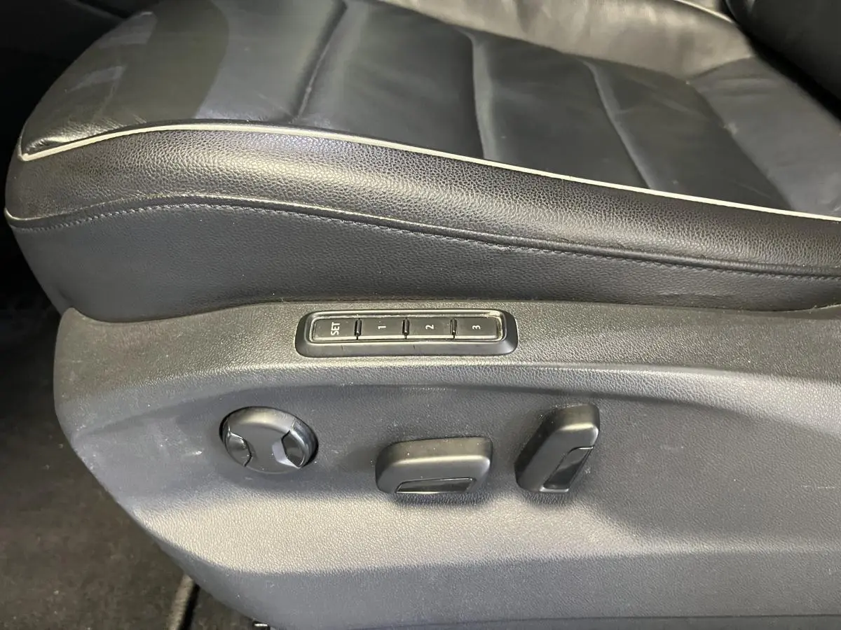 Gros plan sur les commandes de réglage électrique du siège conducteur en cuir noir du Volkswagen Tiguan blanc.