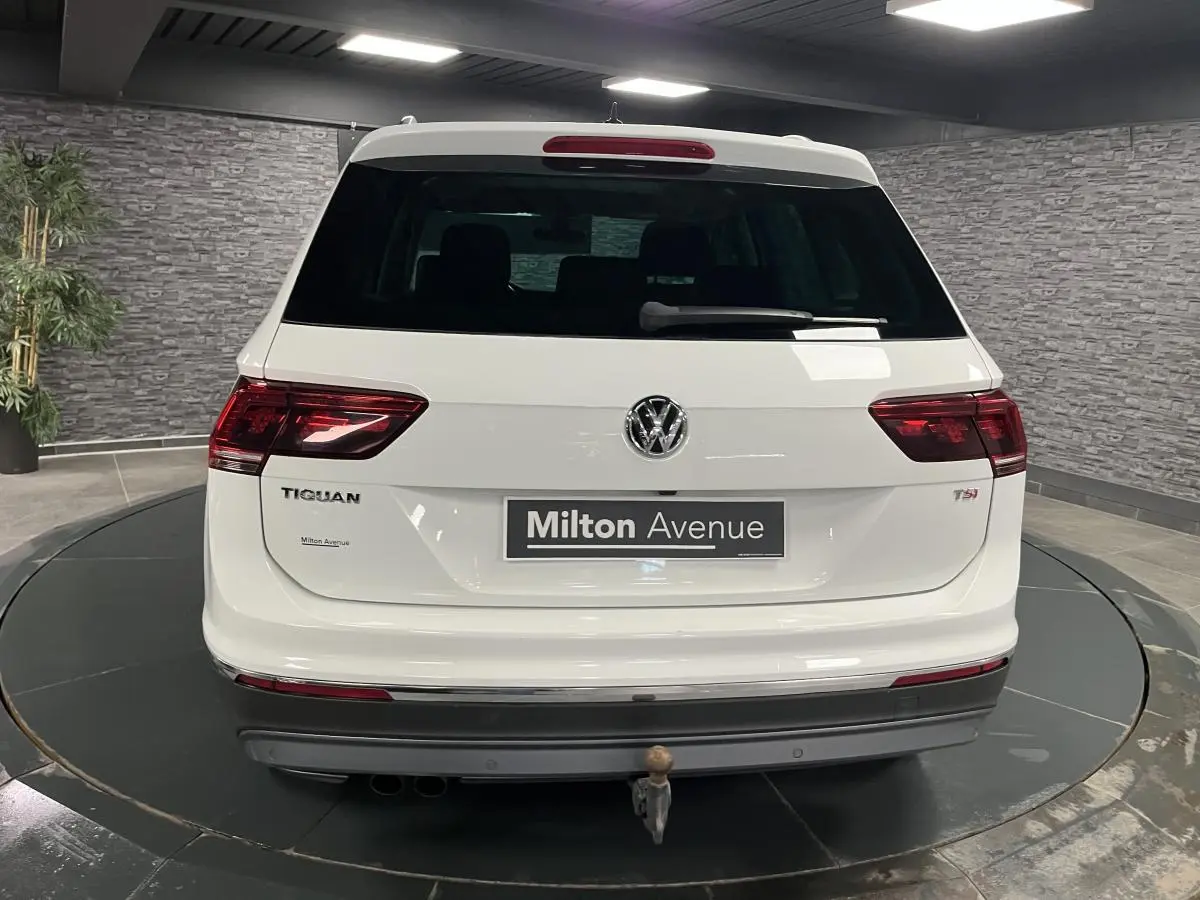 Vue arrière d'un Volkswagen Tiguan blanc avec crochet d'attelage escamotable et feux arrière LED 3D dans un showroom.