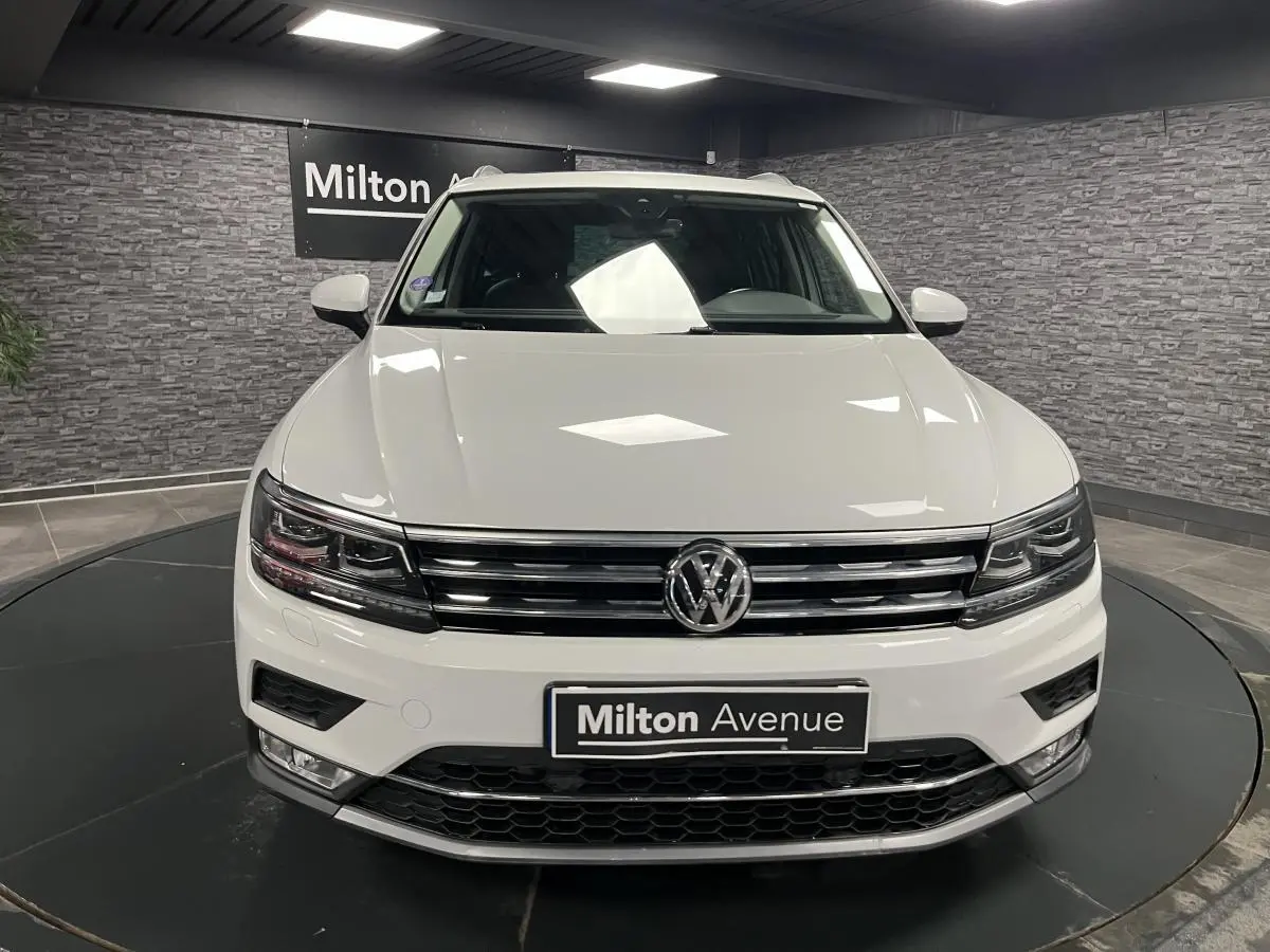 Volkswagen Tiguan blanc vu de face, avec calandre chromée et phares LED dans un showroom intérieur.