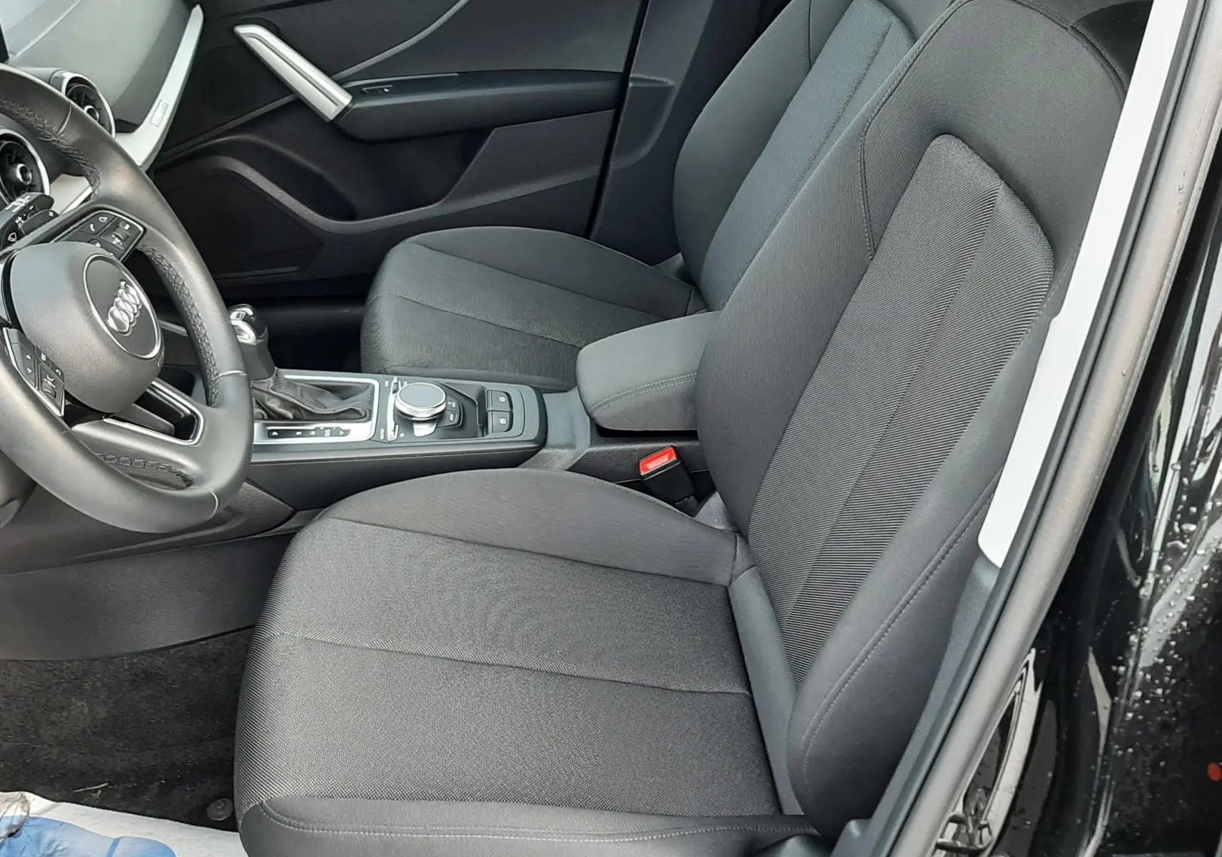 Vue intérieure côté conducteur de l'Audi Q2 2023 noir mito metal, sièges tissu gris et console centrale avec commandes.
