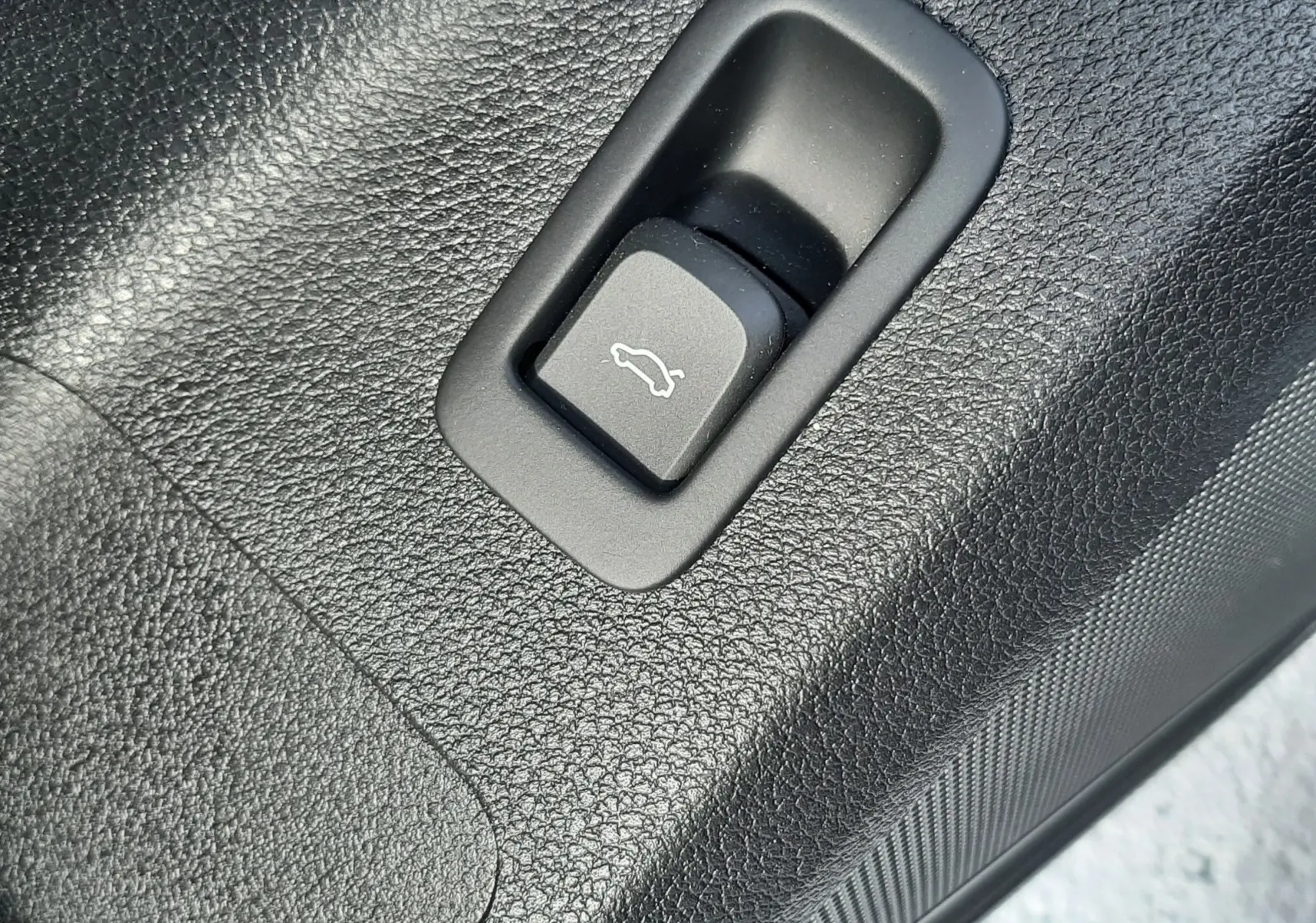 Gros plan sur le bouton d'ouverture de coffre en plastique noir texturé à l'intérieur d'un Audi Q2 noir mito metal 2023.