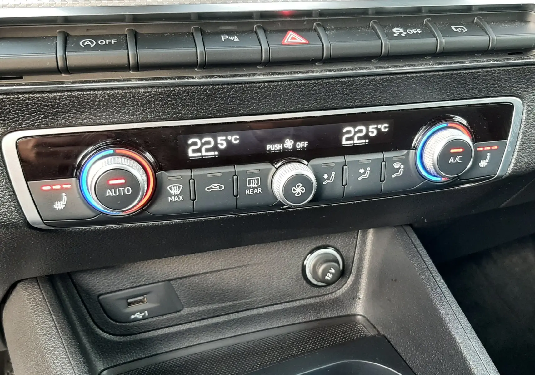 Gros plan sur la console centrale du tableau de bord de l'Audi Q2 noir mito metal, montrant la climatisation digitale et les commandes chauffantes.