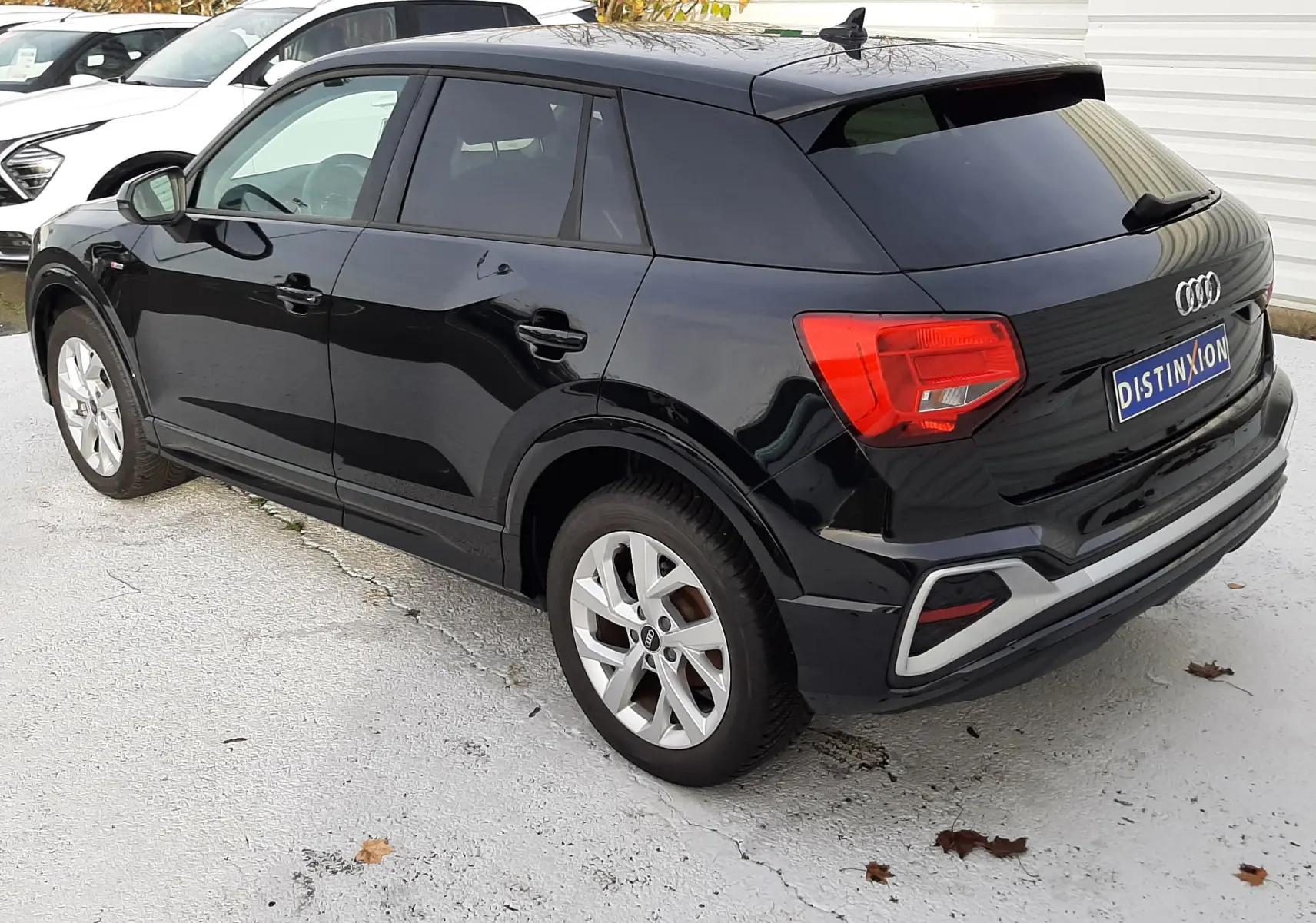Audi Q2 noir mito metal vue 3/4 arrière droit, avec jantes argentées et feux arrière rouges visibles.