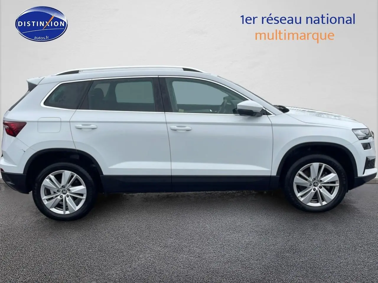 Vue de profil côté gauche d'un Skoda Karoq blanc glacial avec jantes alliage et barres de toit noires.
