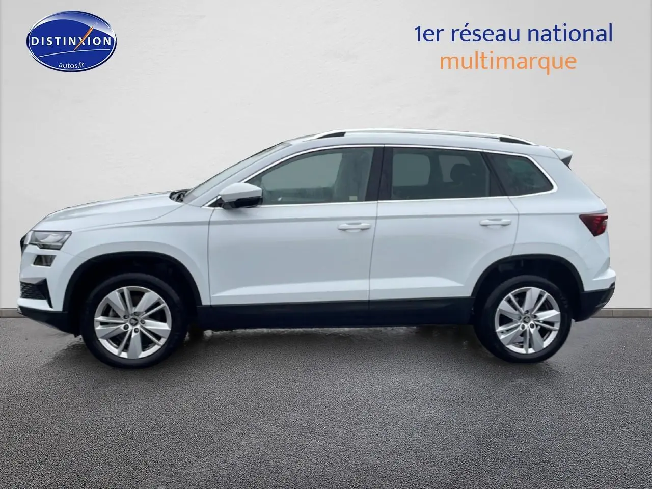 Vue de profil côté gauche d'un Skoda Karoq blanc glacial avec jantes alliage et barres de toit noires.