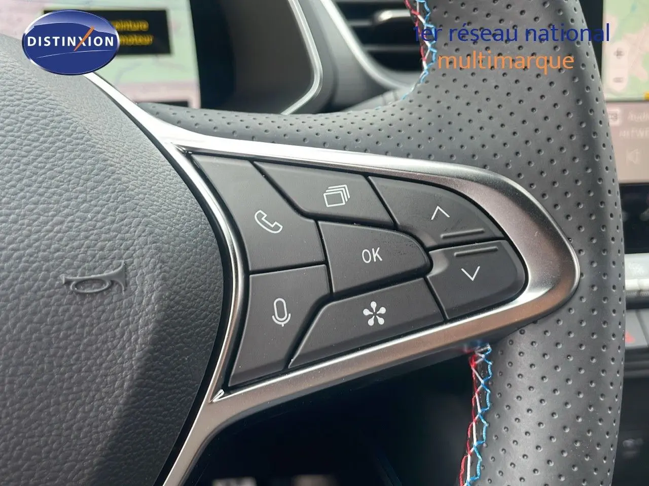 Gros plan sur les commandes au volant perforé avec surpiqûres tricolores du Renault Captur E-Tech hybride 2025 bleu iron metal.