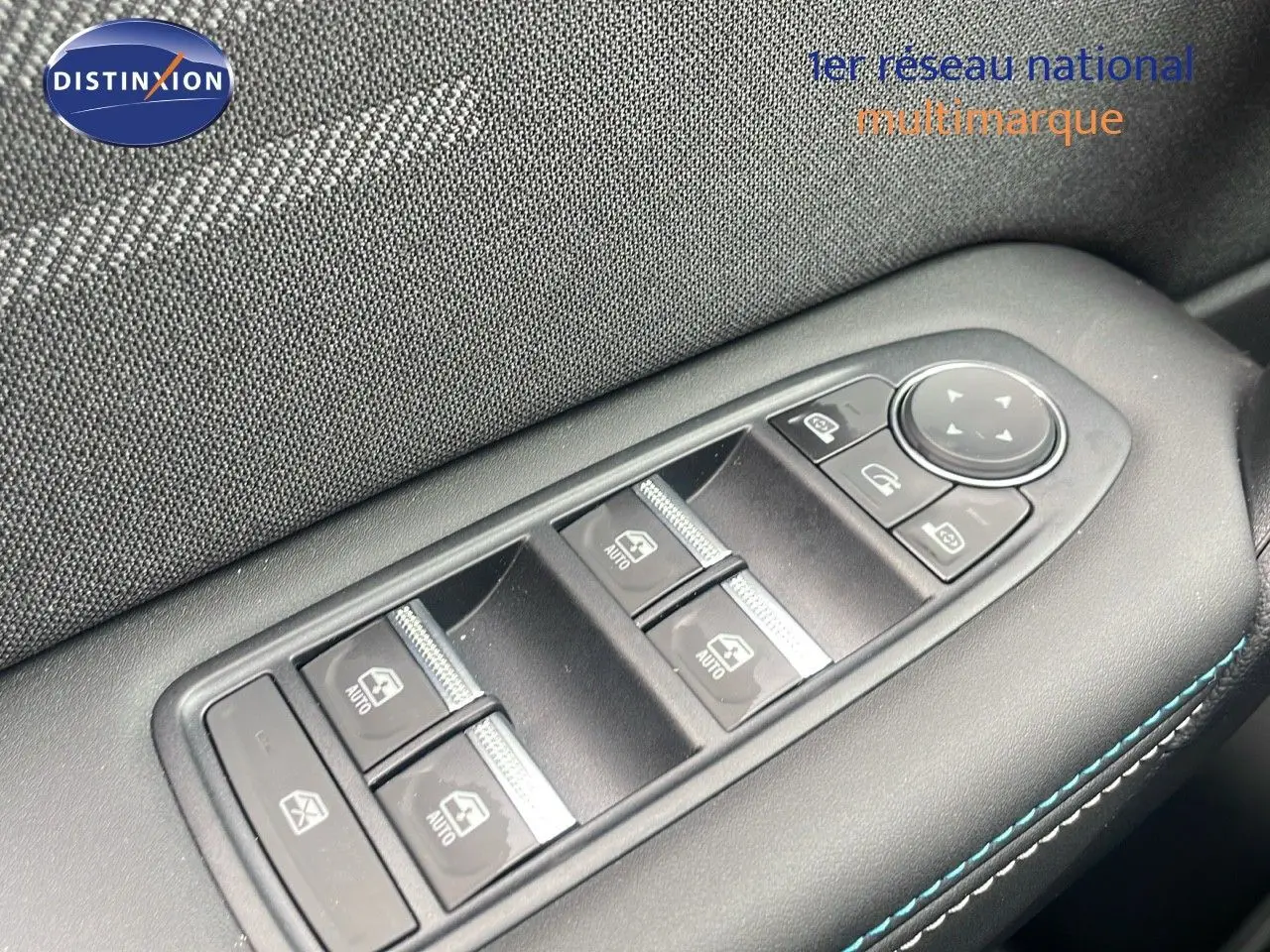 Gros plan sur les commandes des vitres électriques côté conducteur du Renault Captur bleu iron metal avec surpiqûres bleues.