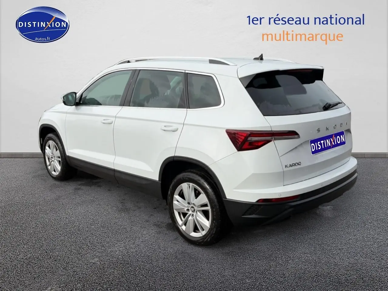 Vue 3/4 arrière droite d'un Skoda Karoq blanc glacial avec jantes alu et barres de toit visibles.