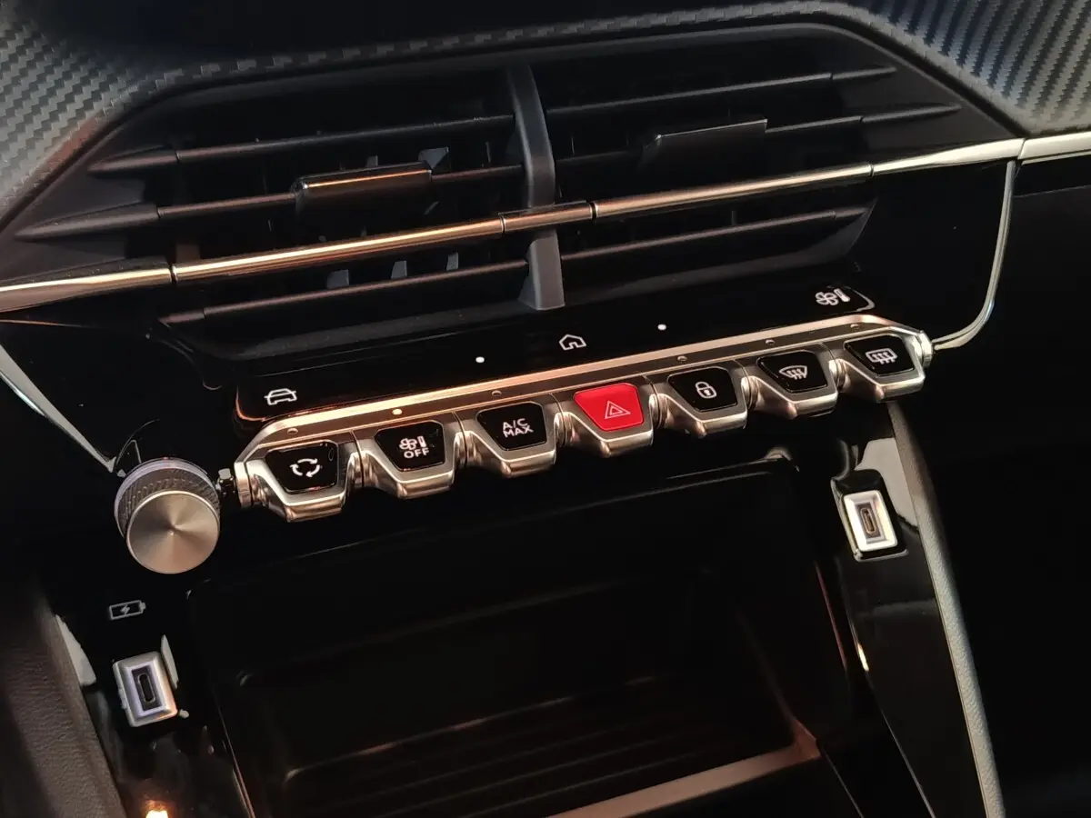Gros plan sur la console centrale noire de la Peugeot 208 Hybrid 2025 avec boutons argentés et rouge d’alerte.