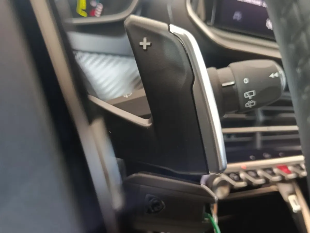 Gros plan sur la palette de changement de vitesse côté droit dans l'habitacle d'une Peugeot 208 gris clair hybride 2025.