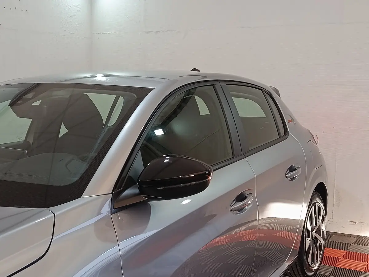 Vue de côté droit avant d'une Peugeot 208 Hybrid gris clair avec rétroviseur noir et jantes distinctives.