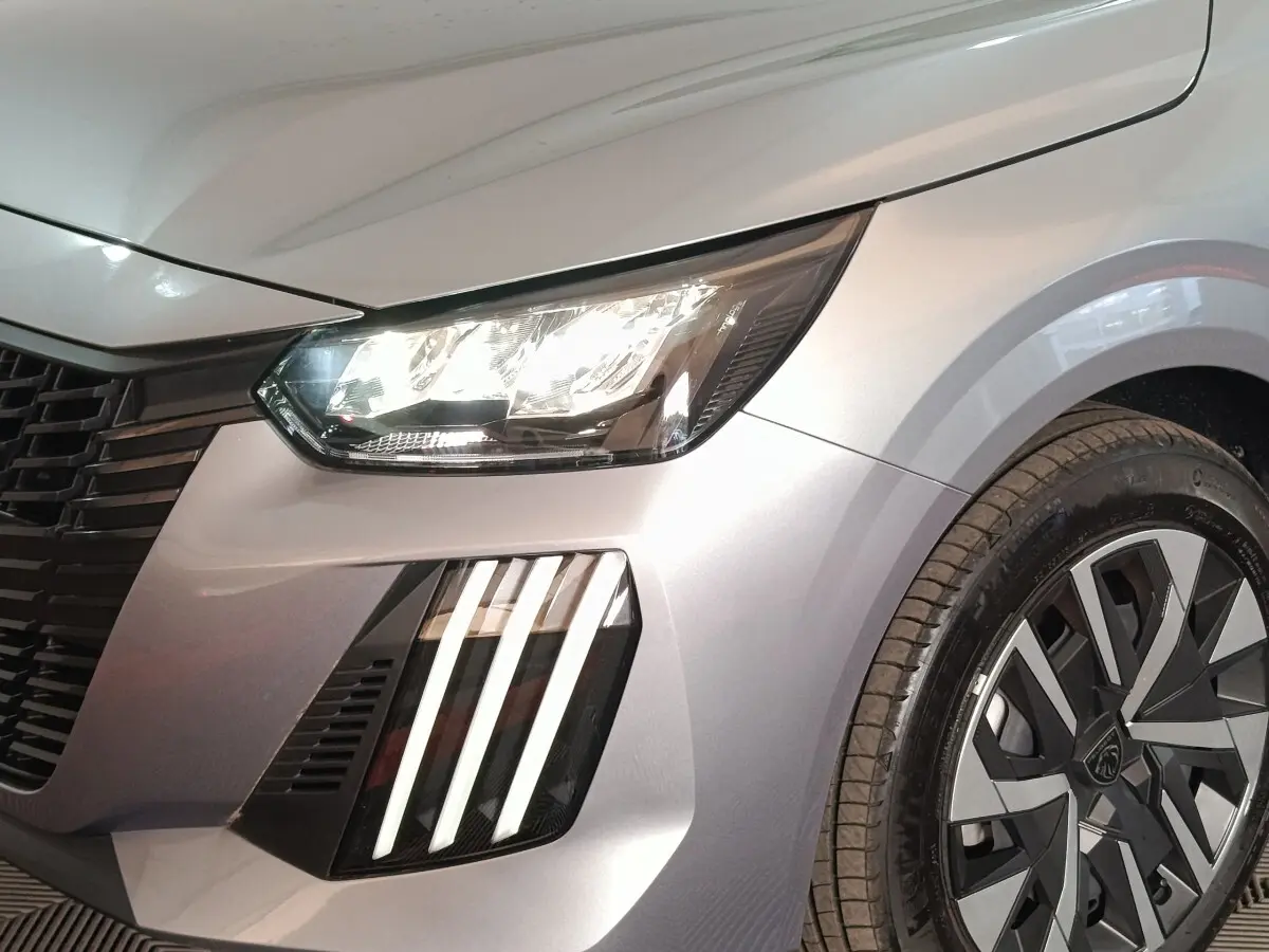 Gros plan sur l'avant droit gris clair de la Peugeot 208 Hybrid 100 avec phares LED et jante au design moderne.