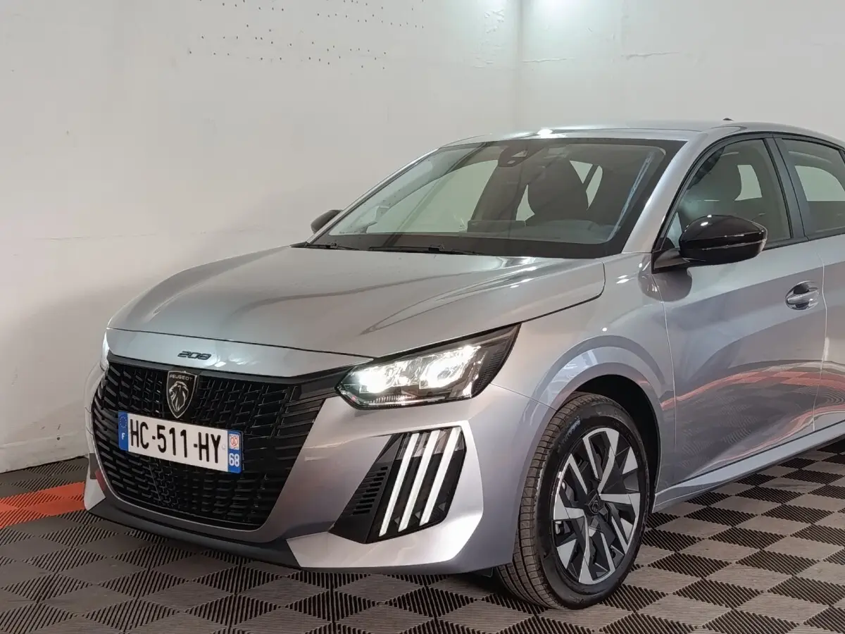 Vue 3/4 avant droit d'une Peugeot 208 Hybrid gris clair avec phares LED et calandre noire distinctive.